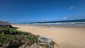 A beach with a wooden bench, a small structure, and the ocean in the background. - Ora Beach poucos passos do mar by LP (Ipojuca)