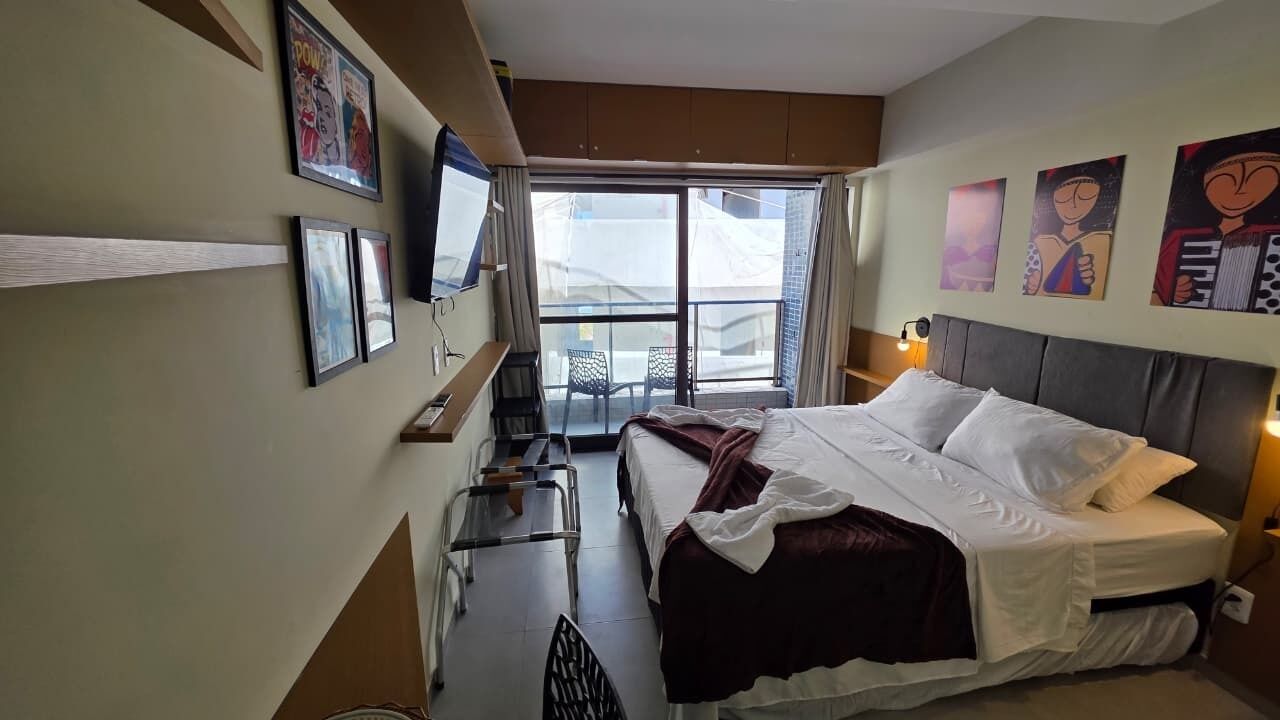 A bedroom with a bed, a TV, a chair, and a window.