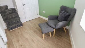Een kamer met een grijze stoel, een houten vloer, een witte deur en een groene wand.