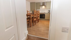 Een trap die leidt naar een eetgedeelte met houten stoelen en een tafel, een keuken met kastjes en een fornuis, en een lichtschakelaar aan de muur.