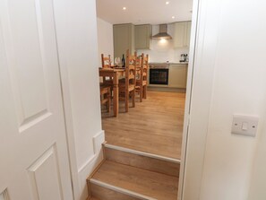 Eine Treppe führt zu einem Essbereich mit Holzkreisen und einem Tisch, einer Küche mit Schränken und einem Herd, sowie einem Lichtschalter an der Wand.