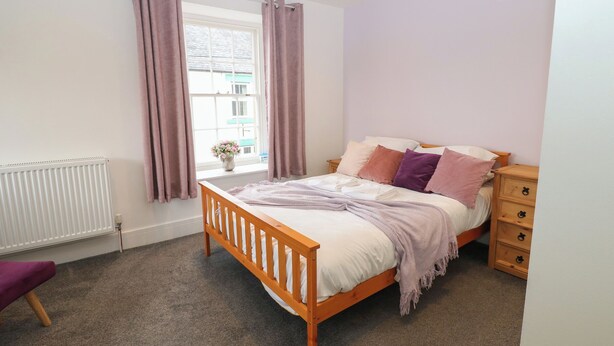 Een slaapkamer met een houten bed, een nachtkastje, een dressoir, een raam met gordijnen en een radiator.