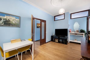 A living room with a white table, yellow chairs, a flat-screen TV, and a framed picture on the wall.