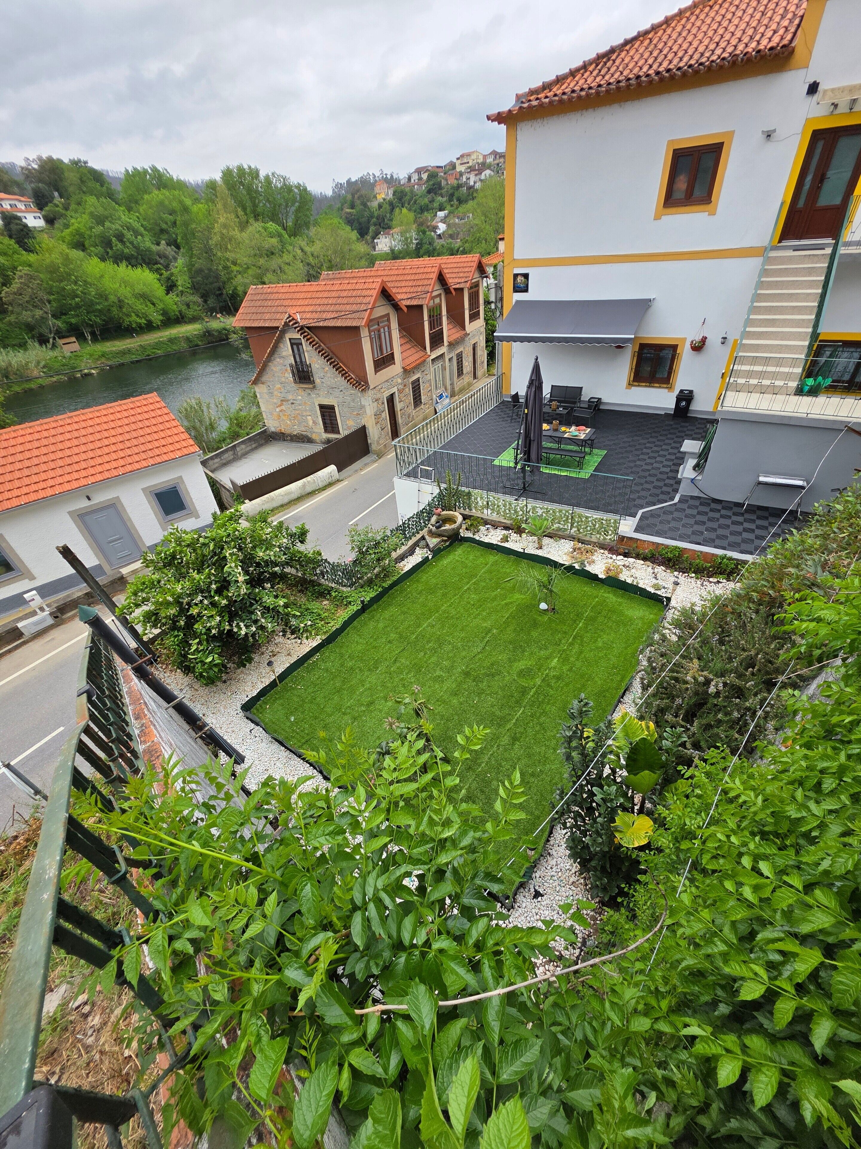 A courtyard with a lawn, a stone building with a red roof, and a white building with yellow trim.