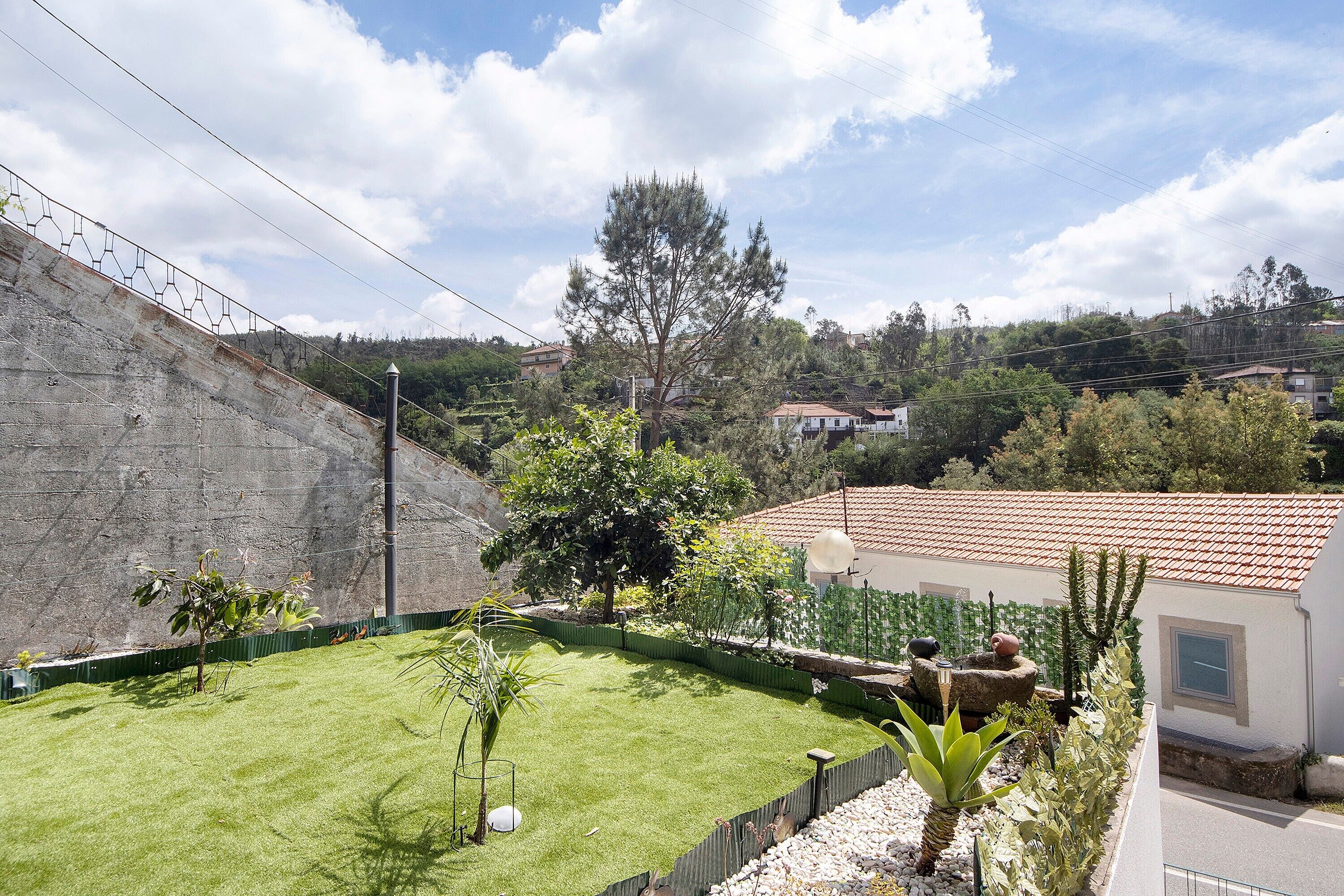 A residential area with a sloped concrete wall, a grassy yard, and a house with a red-tiled roof.