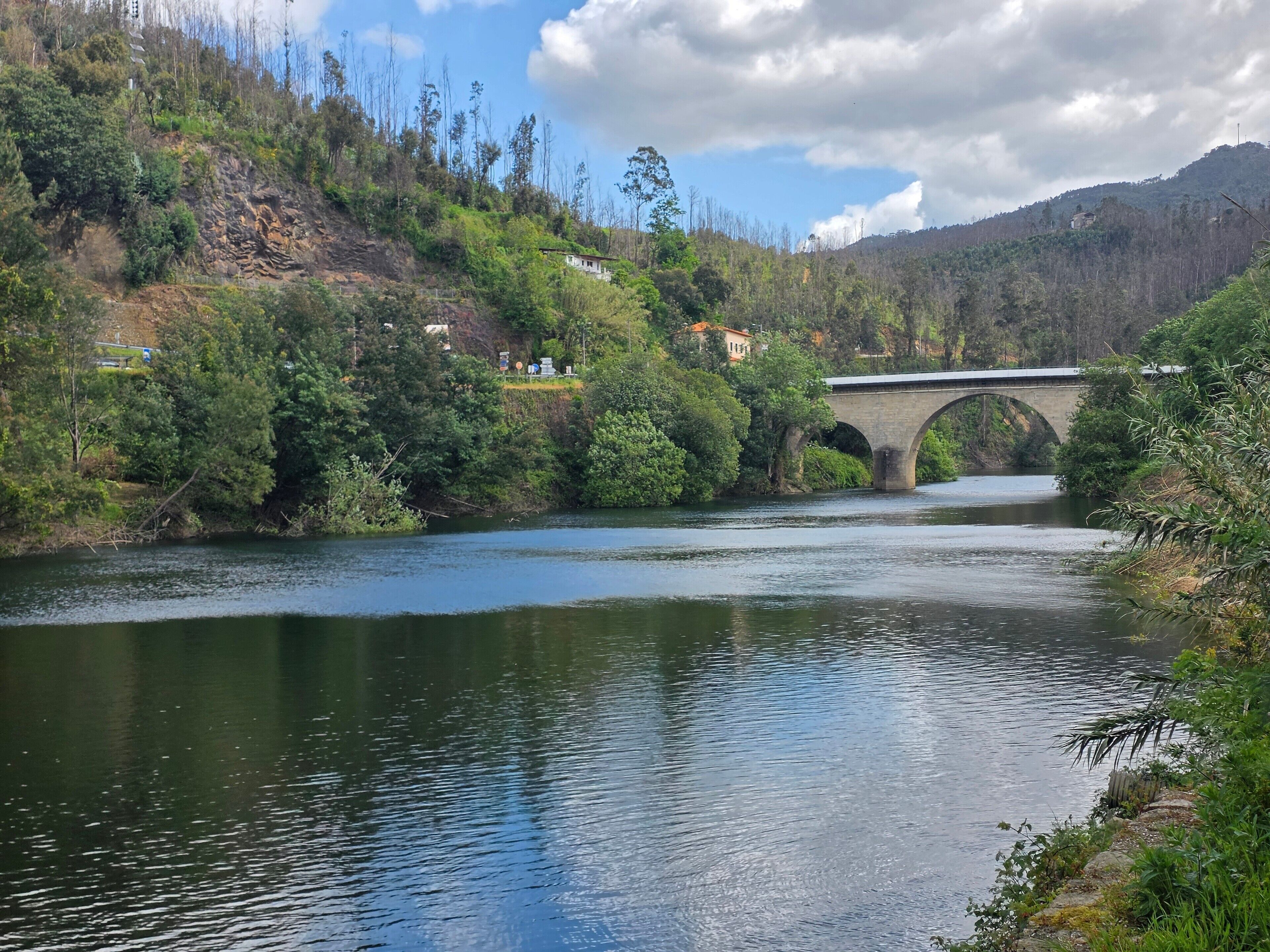 Un río con un puente de piedra, rodeado de vegetación y colinas.