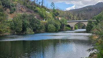 Un río con un puente de piedra, rodeado de vegetación y colinas.