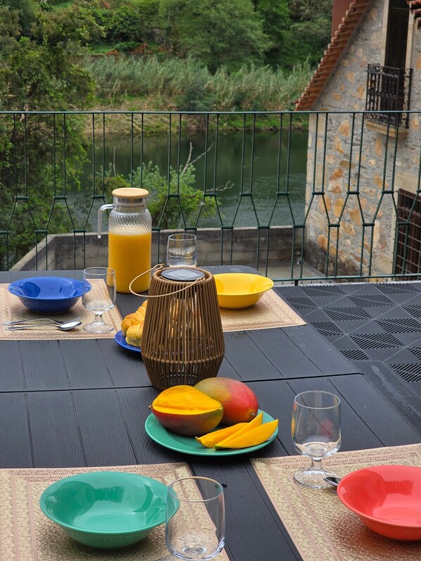 A table set with plates, glasses, a fruit bowl, a bottle, and a candle, overlooking a body of water.