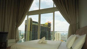 Een hotelkamer met een groot bed, gordijnen, een bureau en uitzicht op een stadsbeeld.