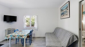 Ein Zimmer mit Esstisch, Stühlen, einer Couch, einem Fernseher und einem Fenster mit Vorhängen.