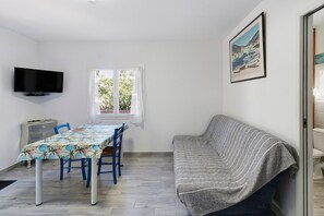 Une pièce comprenant une table à manger, des chaises, un canapé, un téléviseur et une fenêtre avec des rideaux.