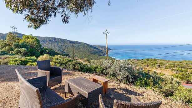 Terrassenmöbel aus Rattan, ein Holztisch und Blick auf die Küste.