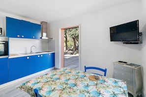 Una cocina moderna con armarios azules, una mesa de comedor con mantel estampado tropical, un televisor montado en la pared y vistas al exterior a través de una puerta de cristal.