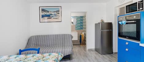 Ein Schlafzimmer mit einem Bett, einer Couch, einer Küchenzeile inklusive Mikrowelle und Backofen sowie einem durch eine offene Tür einsehbaren Badezimmer.
