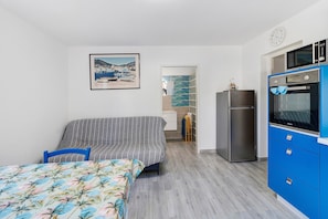 Un dormitorio con cama, sofá, kitchenette con microondas y horno, y un baño visible a través de una puerta abierta.