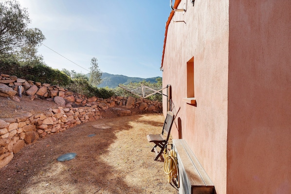 Un espacio exterior rústico con un muro de piedra, un banco de madera y una manguera amarilla.