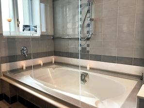 Ein modernes Badezimmer mit einer großen Badewanne, einer Duschkabine aus Glas und einem Spiegel mit Bilderrahmen.
