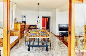 A dining area with a wooden table and chairs, a fireplace, a television, and a view through a glass door.