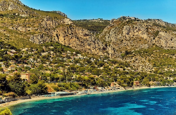 A coastal town with buildings on a hillside, a beach, and a clear blue sea.