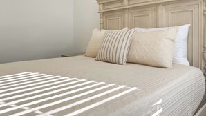 Una cama bien tendida con un edredón estampado y almohadas, un cabecero de madera y una mesita de noche a la izquierda.