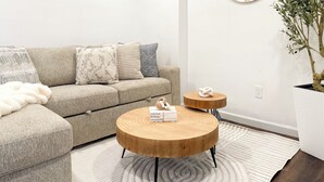 Una sala de estar moderna con un sofá, dos mesas redondas de madera, un reloj de pared y una planta en maceta.