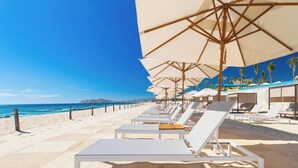 Ein Hotel direkt am Strand mit Liegestühlen, Sonnenschirmen und Blick auf das Meer.