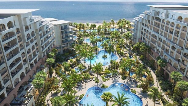 Ein Hotel mit mehreren Etagen, einem zentral gelegenen Swimmingpool, der von Palmen umgeben ist, und Blick aufs Meer.