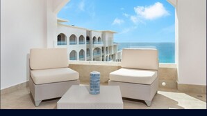 Ein Balkon mit zwei gepolsterten Stühlen und einem kleinen Tisch, mit Blick auf ein Gebäude mit mehreren Balkonen und freiem Meerblick.