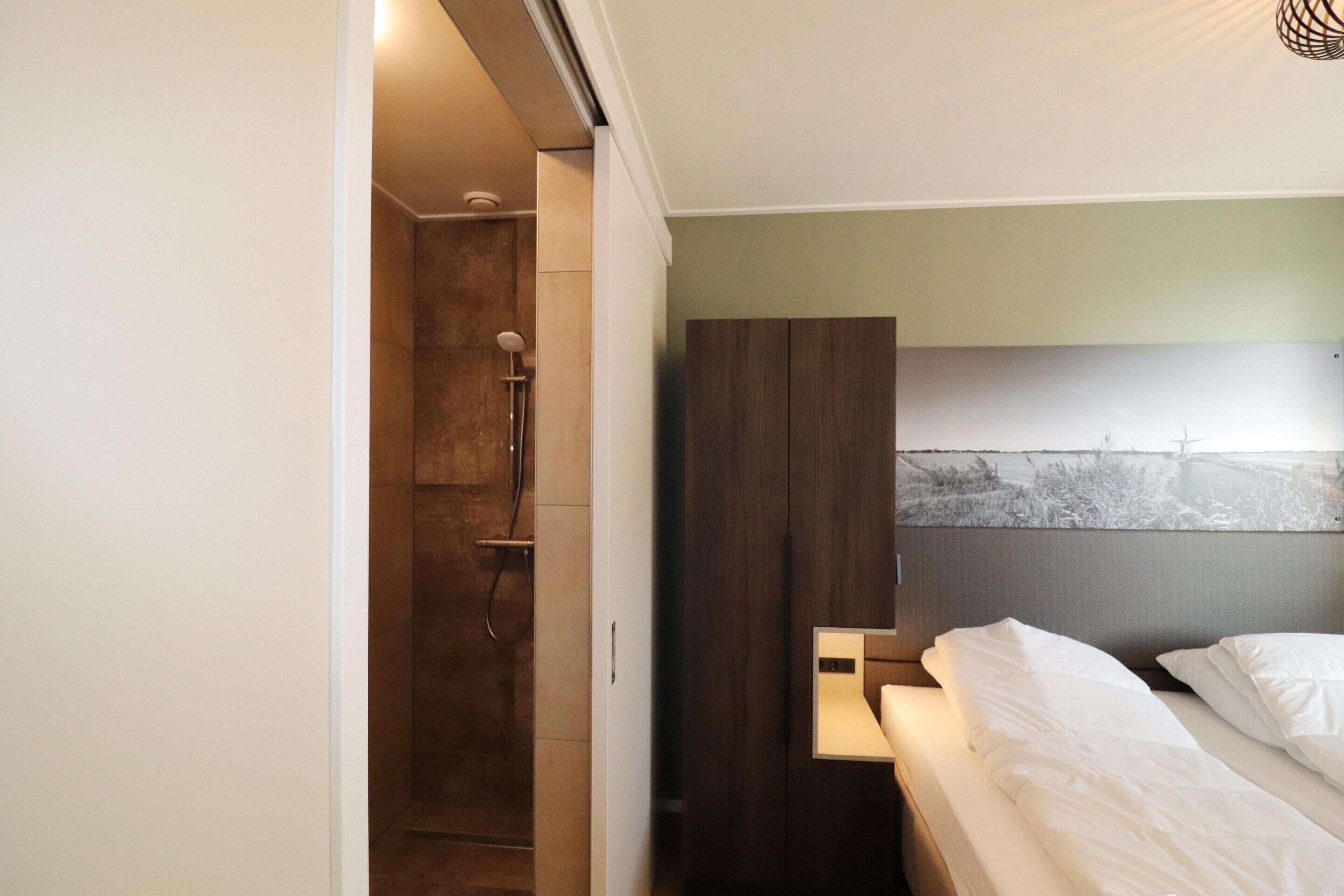 A bedroom with a bed, a nightstand, a wardrobe, and a shower area.