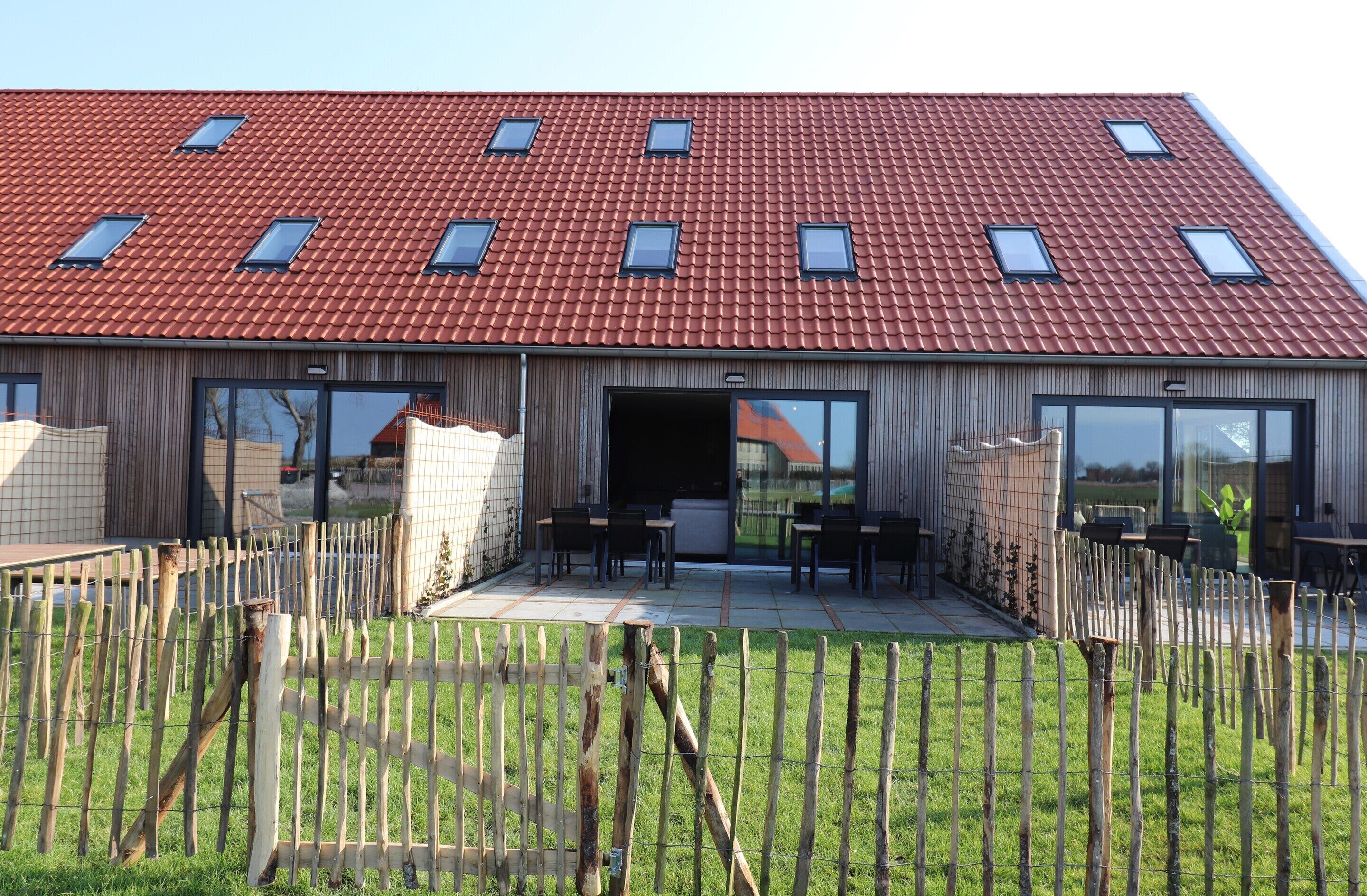 A modern building with a red-tiled roof, large windows, and a fenced outdoor area with seating.