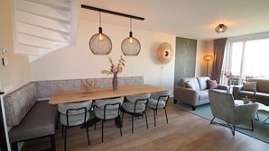 Een moderne woonkamer met een houten eettafel, grijze gestoffeerde zitplaatsen, een bank en een decoratief wandobject.