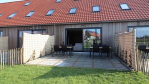 Een modern gebouw met een dak van rode tegels, een overdekt terras met tafels en stoelen, en een omheind gebied.