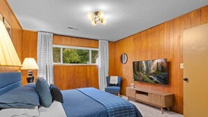 A bedroom with a bed, a TV, a window, and a wooden wall. - Black Diamond | Mid-Century Modern Hot Tub Retreat (Clallam County)