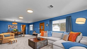A living room with a sofa, armchair, coffee table, and a dining area with a table and chairs. - Black Diamond | Mid-Century Modern Hot Tub Retreat (Clallam County)