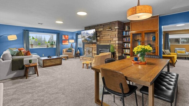 A modern living room with a fireplace, a dining table, and a bookshelf. - Black Diamond | Mid-Century Modern Hot Tub Retreat (Clallam County)