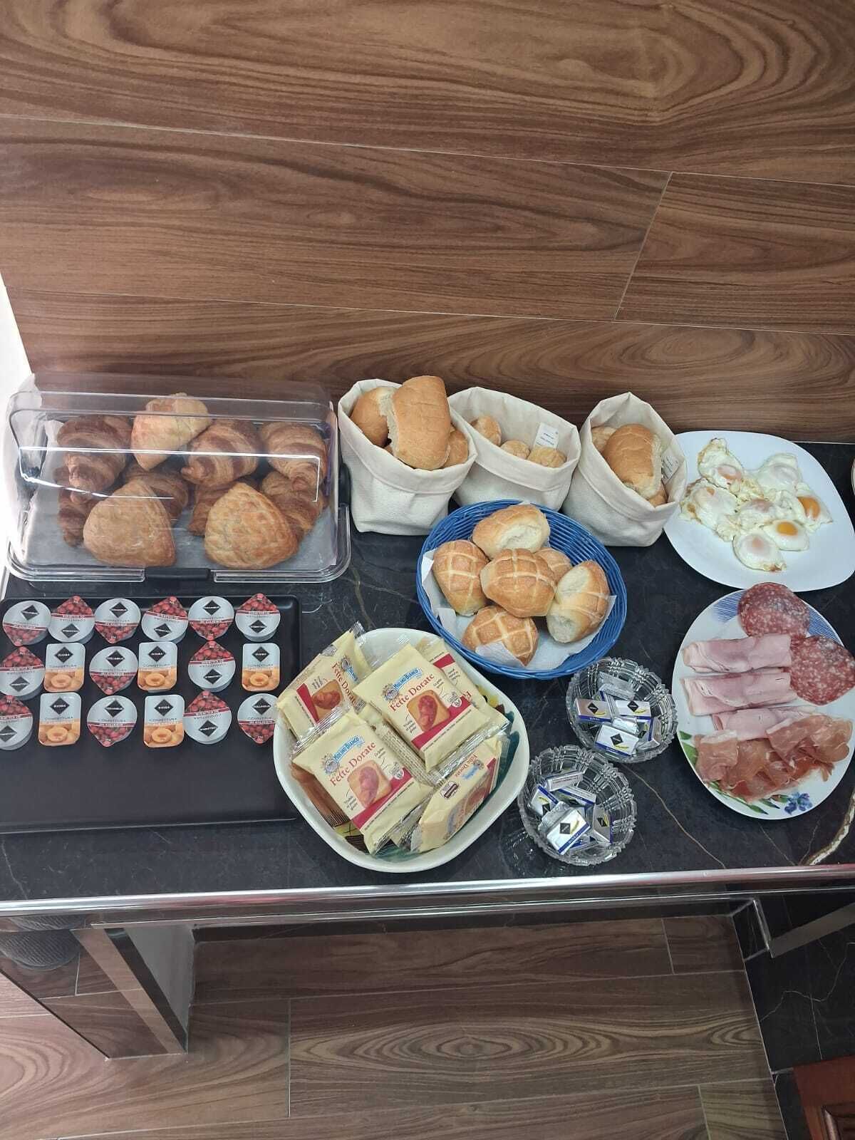 A buffet table with various food items including pastries, bread, and deli meats.