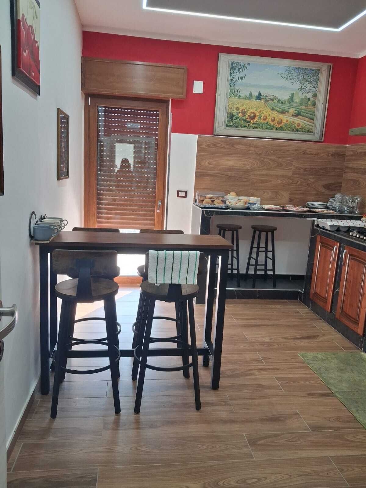 A dining area with a wooden table and chairs, a kitchen with a stove, and a painting on the wall.