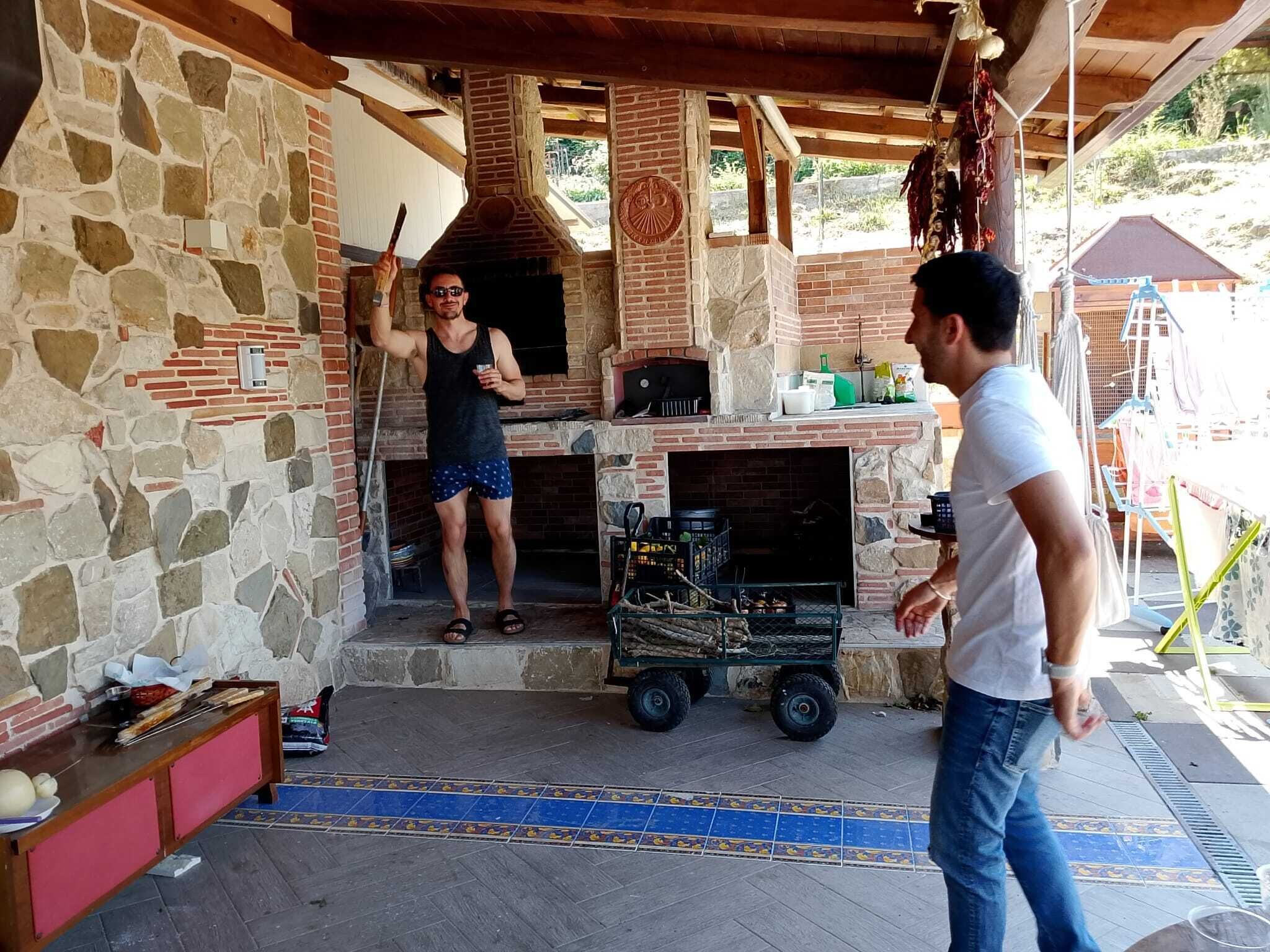 Un área de cocina exterior de piedra y ladrillo, con chimenea, un hogar y un carrito con utensilios para asar.