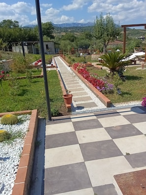 A garden pathway with a checkered floor leading to a seating area, surrounded by greenery and potted plants. - PINK VILLA (Contursi Terme)