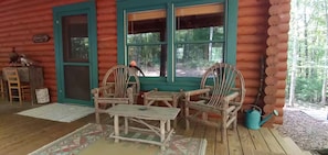 A log cabin with a porch, wooden chairs, a table, and a birdhouse. - Cozy Cabin w King, 8-Stall Barn/Borders Big South Fork Natl Park, Pet-Friendly (Oneida)