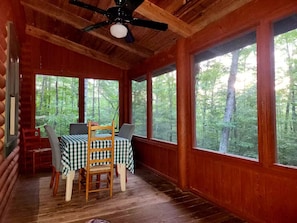A cabin interior with a wooden ceiling, a table with a checkered tablecloth, and large windows offering a forest view. - Cozy Cabin w King, 8-Stall Barn/Borders Big South Fork Natl Park, Pet-Friendly (Oneida)