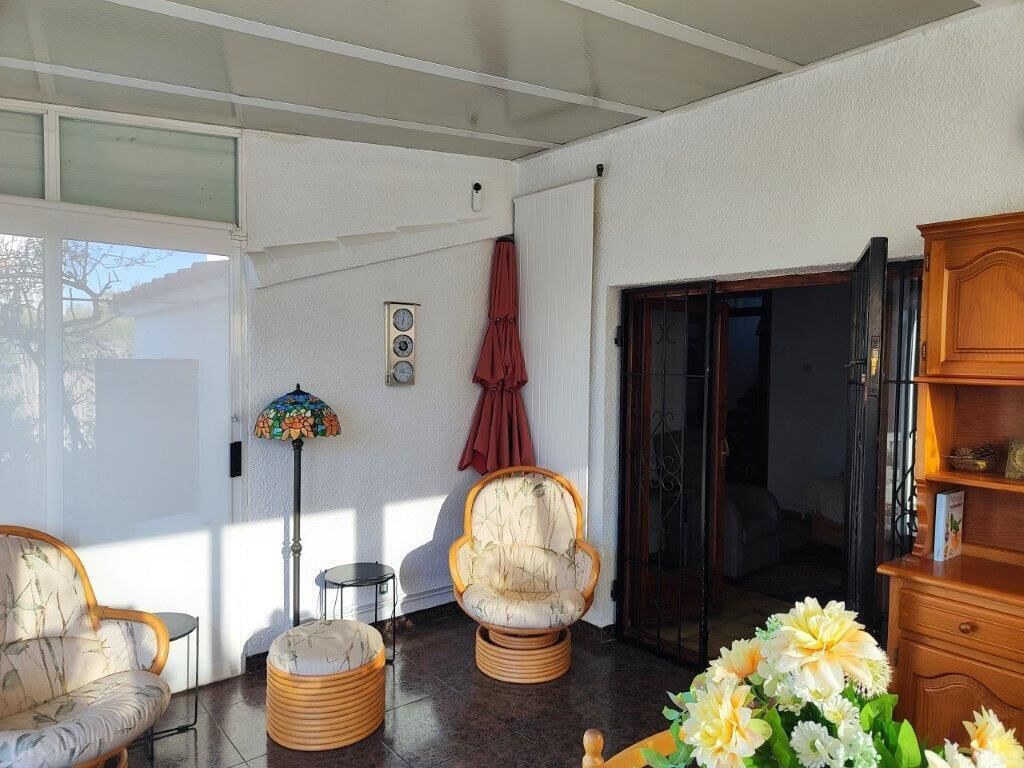 A sunlit room with a sofa, armchairs, a floor lamp, a wooden cabinet, and a door leading outside.