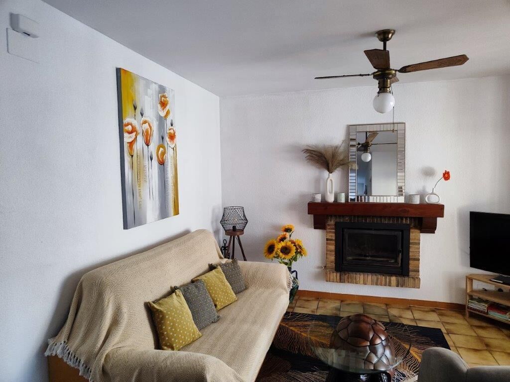 Un salon avec un canapé, une cheminée, un ventilateur de plafond et un tableau accroché au mur.