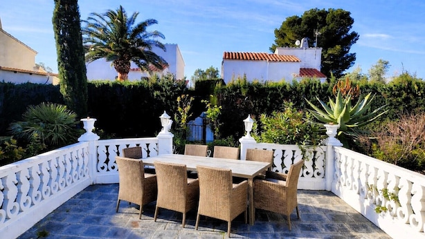 Une terrasse extérieure avec une table et des chaises, entourée de balustrades blanches et de verdure.