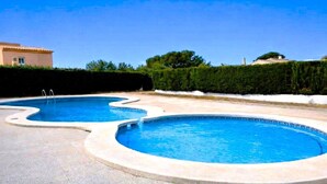 Une piscine au design incurvé, entourée d’une zone pavée et d’une haie.