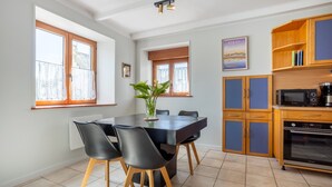 Un coin repas comprenant une table, des chaises, un vase avec des plantes, et une cuisine équipée d’armoires et d’appareils électroménagers.