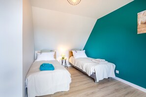 A room with two beds, a teal accent wall, and a wooden floor.