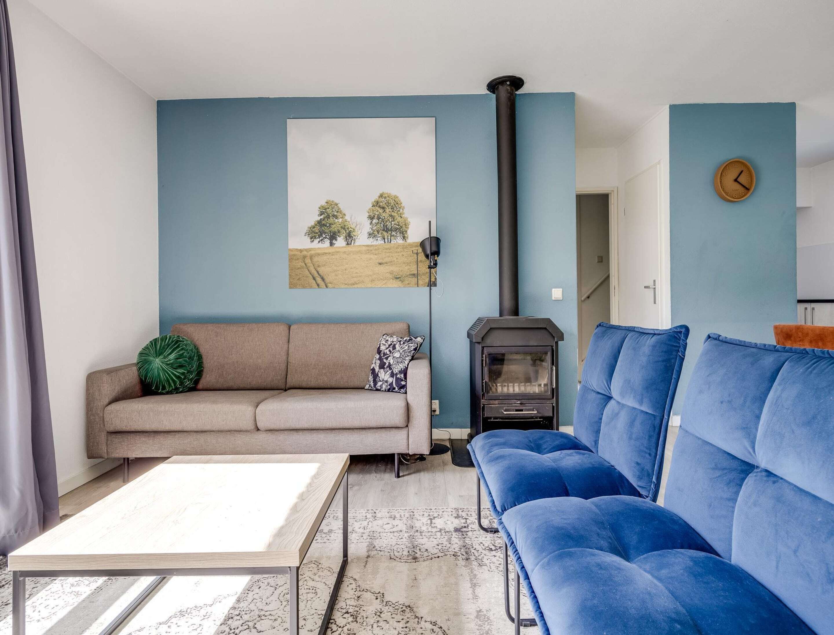 A living room with a sofa, a blue couch, a table, a fireplace, and a painting on the wall.