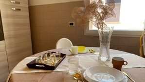 Uma mesa de jantar posta com uma bandeja de copos, um copo de vidro transparente, um prato branco, uma colher dourada, uma caneca marrom e um vaso decorativo.