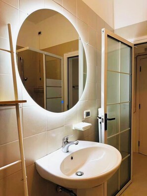 A bathroom with a round mirror, a sink, and a glass shower enclosure.